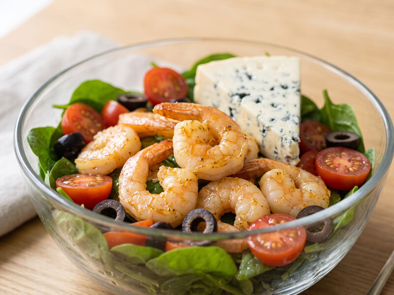 Close-up of finished keto buttered shrimp salad with shrimp, spinach, tomatoes, olives, and blue cheese.